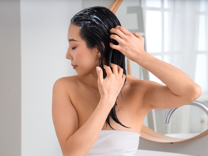 A woman applying leave-in conditioner to her hair.