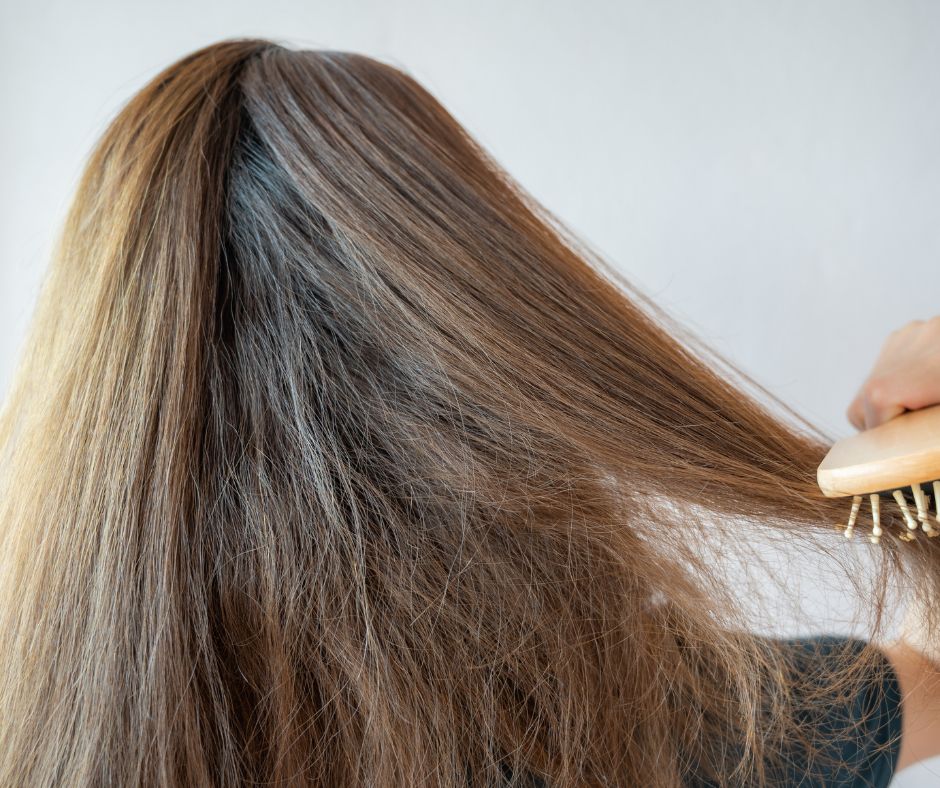 A woman is combing her thick, dry hair.